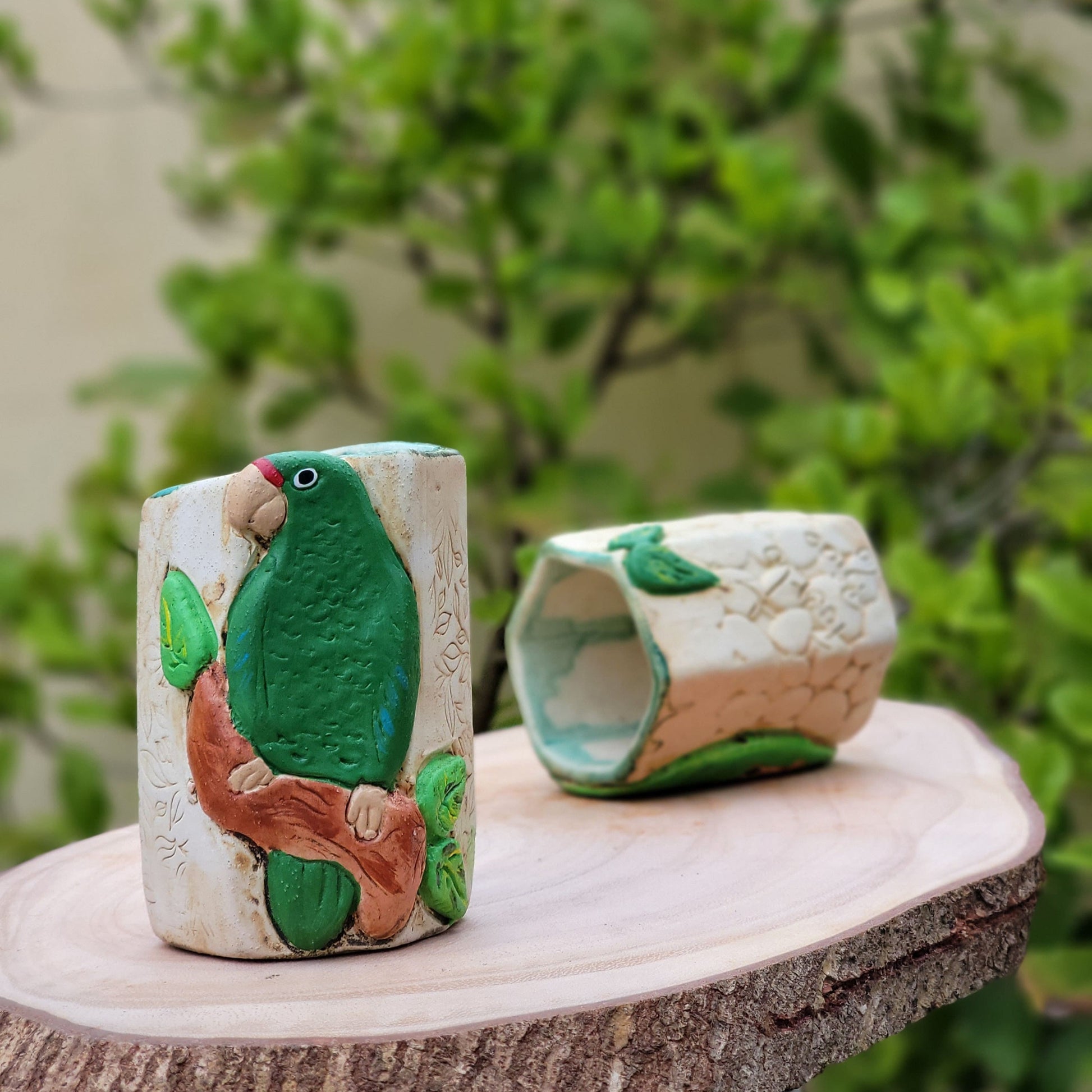 Decorative ceramic parrot figurines on a natural stone surface with greenery in the background