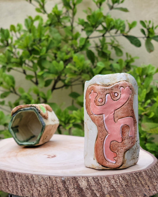 Ceramic holder object with a textured surface, set against a blurred green outdoor background.